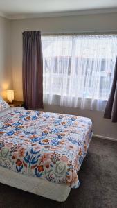 Un dormitorio con una cama con una manta de flores y una ventana en Bowmont, en Invercargill