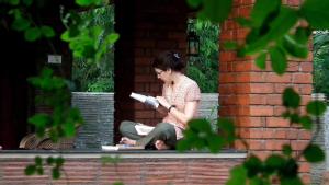 a woman sitting on a bench reading a book at Clayfingers Art Cottage in Trichūr