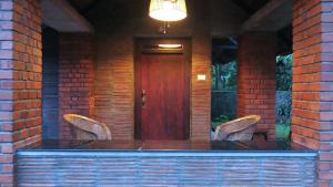 a porch with two chairs and a wooden door at Clayfingers Art Cottage in Trichūr