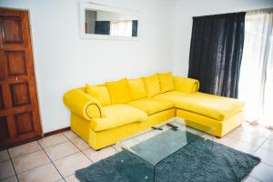 a yellow couch in a living room with a glass table at Ankazimia House at Reeds View in Roodepoort