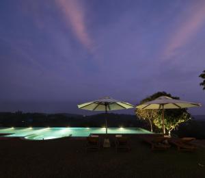 two umbrellas and chairs next to a swimming pool at night at Heavensa Luxury Villas in Galle