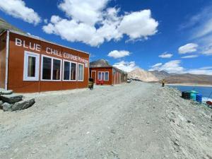 a building on a dirt road next to a body of water at Blue Chill Cottage Pangong in Lukung