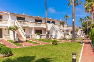 un grand bâtiment blanc avec des palmiers et une pelouse dans l'établissement Apartamento en complejo de zonas ajardinadas-c11, à Ciutadella