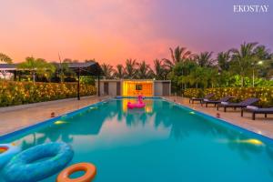 een zwembad met roze opblaasbare bedden in een resort bij EKOSTAY Luxe - Woodstock Villa I 2 Acre Property I Cricket Turf I Party Friendly in Karjat