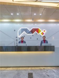 Dos personas sentadas en un escritorio en una habitación en Borrman Hotel Kunming Dianchi South Asia Fengqingyuan en Kunming