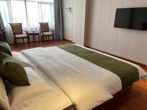 GreenTree Alliance Hotel Jiangsu Suzhou Xiangcheng Distrcit Dongqiao في Sangshubang: غرفة نوم بسرير كبير مع تلفزيون على الحائط