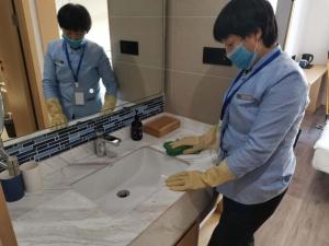 una mujer con una máscara y guantes limpiando un fregadero en Starway Hotel Hangzhou Yipeng Shopping Center, en Chang-shen-tien