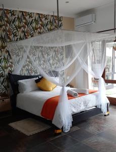 1 dormitorio con cama con dosel y cortinas blancas en Lagoon Ndziva, Bilene, en Vila Praia Do Bilene