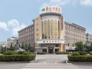 Vienna Hotel Jiangxi Shangrao Yiyang Railway Station Fangzhimin Avenue في Yiyang: مبنى كبير مع برج الساعة في موقف للسيارات