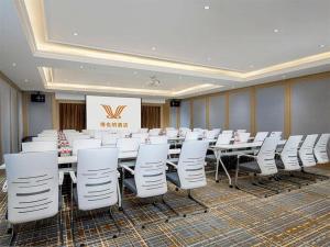 Vienna Hotel Tianjin Binhai New District Ocean High-Tech Zone في Binhai: قاعة المؤتمرات مع صفوف من الطاولات والكراسي البيضاء