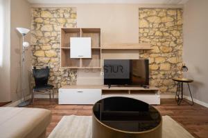 Vive Oviedo II Apartamento في أوفِييذو: غرفة معيشة مع تلفزيون وجدار حجري