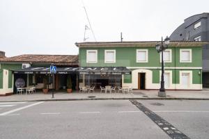 Vive Oviedo II Apartamento في أوفِييذو: عمارة خضراء فيها طاولات وكراسي على شارع