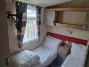 a small room with two beds and a window at 8 BERTH Deluxe caravan PALM GROVE 142 GOLDEN PALM CHAPEL ST LEONARDS in Chapel Saint Leonards