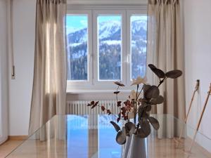 un jarrón con flores en una mesa de cristal frente a una ventana en Airolo Valley Apartments by Quokka 360 - Cozy with Mountain View, en Airolo