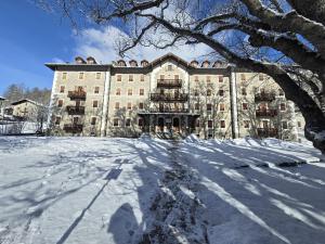 un gran edificio en la nieve con un árbol en Grand Hotel Ceresole Reale studio apartment, en Ceresole Reale
