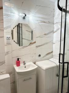 a white bathroom with a sink and a mirror at Coser Apartamenty ONZ in Warsaw