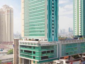 a tall green building in a city with buildings at Novotel Jakarta Gajah Mada in Jakarta