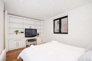 a white bedroom with a bed and a television at Central 2 Bed Maissonette in London