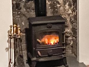 a wood stove with a fire in a room at Smithy End in Chard