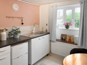 cocina con armarios blancos, fregadero y ventana en Smithy End en Chard