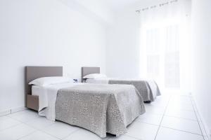 2 camas en una habitación blanca con suelo blanco en Vuelle Residence Apartments, en Capo dʼOrlando