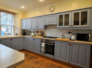 a kitchen with white cabinets and a clock on the wall at The House on the Square- Coastal Townhouse in Saint Monance