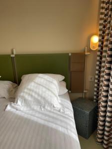 a bed with a green headboard and white pillows at Hotel des Victoires - Restaurant in Cannes