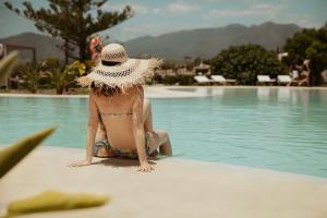 kobieta w kapeluszu siedząca obok basenu w obiekcie La Zambra Resort GL, part of The Unbound Collection by Hyatt w mieście Mijas