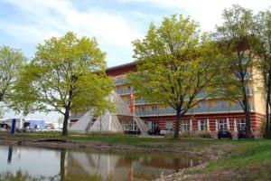 a red building with a building with trees and a pond at Kurhotel Pyramide AG in Bad Windsheim