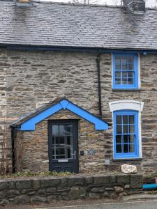 een stenen huis met blauwe ramen en een deur bij Bwthyn Heddwch - Peace Cottage in Machynlleth