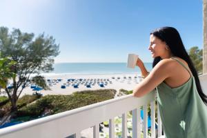 eine Frau, die eine Tasse Kaffee auf einem Balkon mit Blick auf den Strand hält in der Unterkunft RumFish Beach Resort by TradeWinds in St Pete Beach