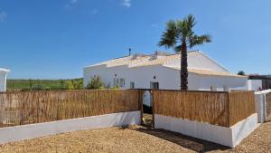 a fence in front of a white house with a palm tree at Milagres de Santa Rita in Vila Nova De Cacela