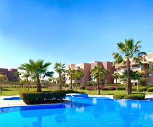 une grande piscine bleue avec des palmiers en face d'un bâtiment dans l'établissement Prestigia Golf entrée Agate (wifi), à Marrakech