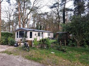 Ruim Chalet, midden in het bos! في نونسبيت: منزل صغير مع دراجة متوقفة أمامه