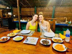 dos mujeres sentadas en una mesa con platos de comida en Sheran Safari House, en Udawalawe
