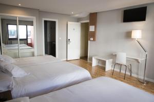 a bedroom with two beds and a desk and a television at Hotel Mogay in Chantada