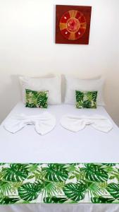 1 cama blanca con 2 almohadas y una foto en la pared en Pousada Portal dos Coqueirais en Jequiá da Praia