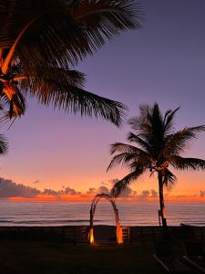 a palm tree and an arch on the beach at sunset at Pousada Quintal Caraíva in Caraíva