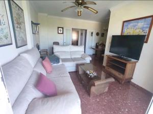 uma sala de estar com sofás brancos e uma televisão de ecrã plano em Piso primera línea de playa em Chipiona