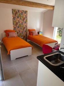 2 Betten mit orangefarbener Bettwäsche in einem Zimmer mit Waschbecken in der Unterkunft La villa Rosa in Bédoin