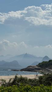 einen Strand mit Meer und Bergen im Hintergrund in der Unterkunft Flat com vista para o mar em Camboinhas in Niterói