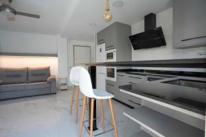 eine Küche mit zwei weißen Barhockern und einem Sofa in der Unterkunft Cómodo apartamento en Playa Gandia in Los Mártires