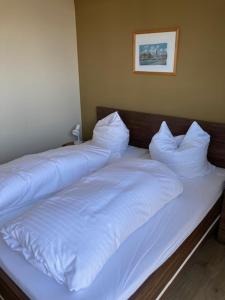 uma cama com lençóis brancos e almofadas em Ferienwohnung Troge em Greifswald