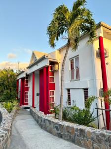 ein rot-weißes Gebäude mit einer Palme in der Unterkunft Résidence Le Vallon Guadeloupe Parc Piscine Appartements & Studios & Services hôteliers à la carte in Saint-François