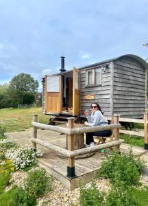 a woman sitting on a fence in front of a trailer at Under the Stars Shepherds Huts at Harbors Lake in Newchurch