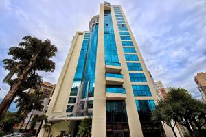 a tall building with glass windows and palm trees at Suíte 5 estrelas Hotel Av Ibirapuera 2534 Moema - 1 in Sao Paulo