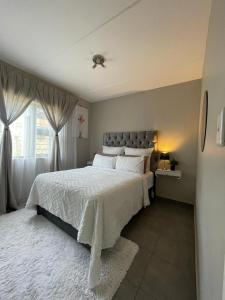 Saffron Place @ 2bed Apt Midrand في ميدراند: غرفة نوم بسرير كبير مع شراشف بيضاء ونافذة