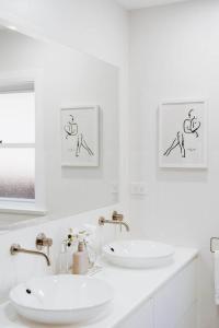 a white bathroom with two sinks and two pictures on the wall at 'Haylock' Luxe Country Charm in Mudgee's Centre in Mudgee