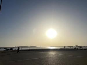 une personne se promenant sur la plage avec le soleil dans le ciel dans l'établissement La Symbiose Essaouira, à Essaouira