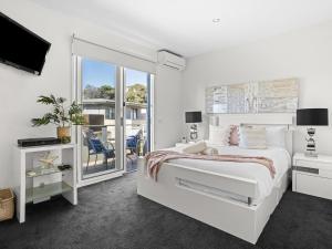 a white bedroom with a bed and a balcony at Koonya Getaway in Sorrento